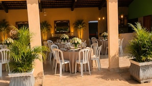 An outdoor patio with round tables, white chairs, and potted plants.