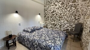A bedroom with a bed, a chair, a small table, a stone wall, and two wall-mounted lights. - ROMY - DAX - City Break (DAX)