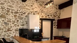 A kitchen with a stone wall, a wooden bar counter, and black bar stools. - ROMY - DAX - City Break (DAX)