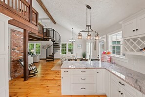 A spacious kitchen with white cabinets, a marble countertop, and a wooden staircase. - East Dennis Gem: 5BRs, Sleeps 12 & Steps to Beach (Dennis)