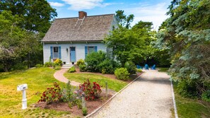 Uma casa com entrada por cascalho, caixa de correio e um pequeno jardim com flores vermelhas.