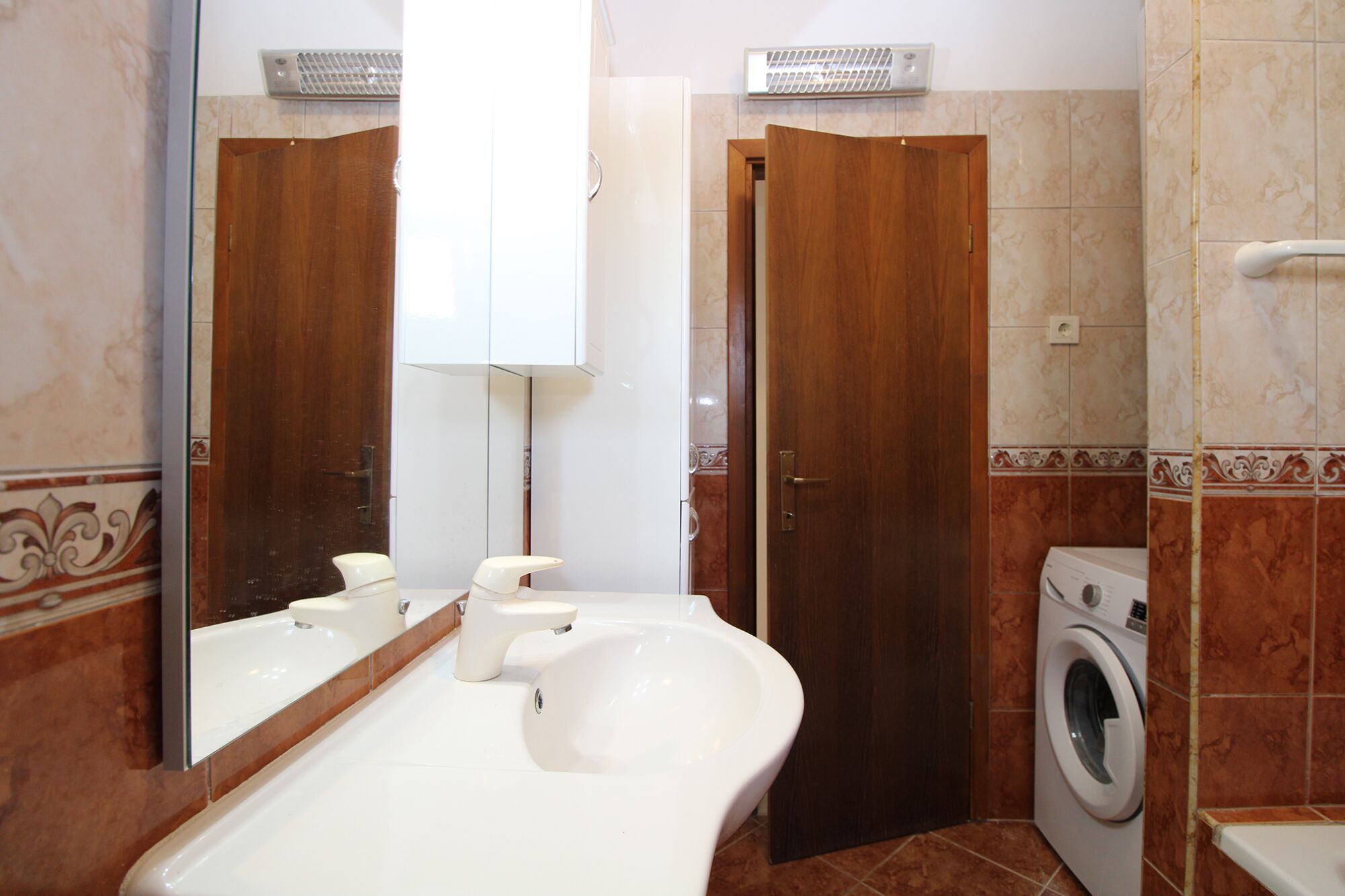 A bathroom with a sink, mirror, toilet, and washing machine.
