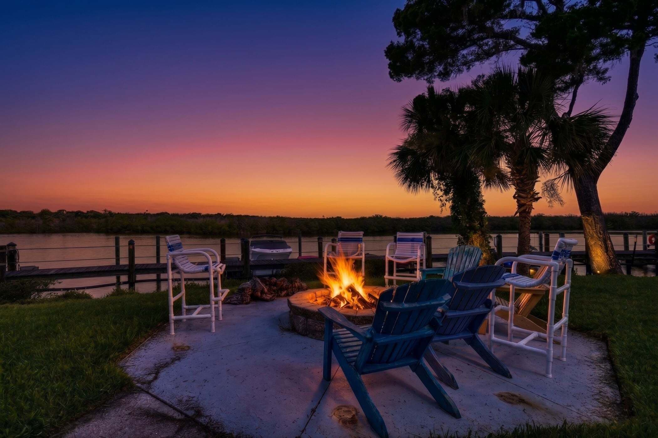 A fire pit with chairs around it, a view of a body of water, and a sunset.
