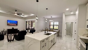 Une cuisine moderne dotée d’un îlot en marbre, de luminaires suspendus et d’une grande fenêtre.