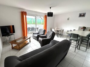 Una sala de estar moderna con un sofá, sillas, un televisor y un comedor con mesa y sillas.