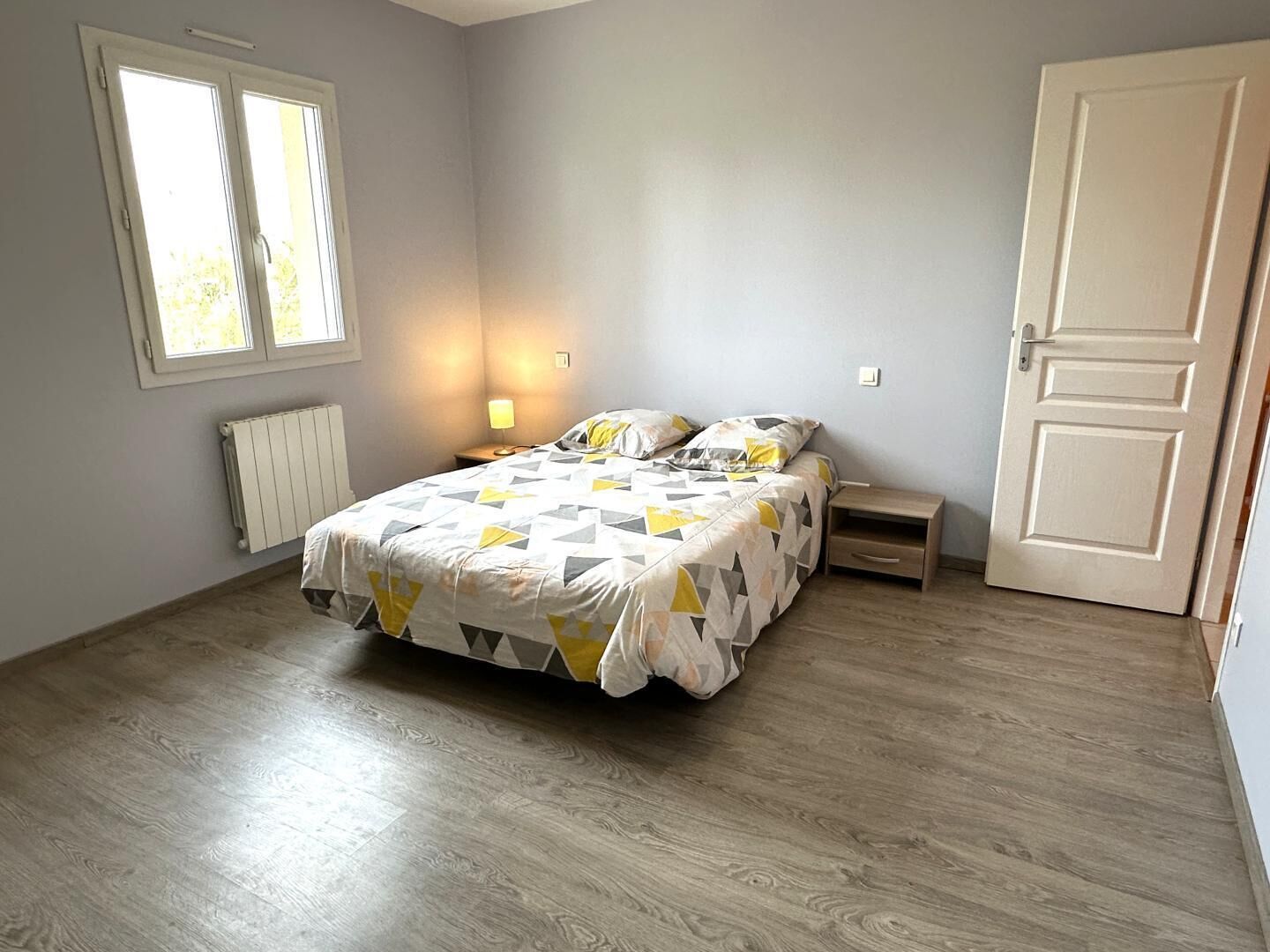 A bedroom with a bed, bedside tables, a radiator, and a door.