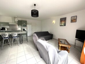 Una sala moderna con un sofá, un comedor con sillas, una cocina equipada y un televisor.