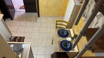 Une cuisine compacte avec un coin repas, une petite table avec des assiettes bleues, une chaise jaune et un réfrigérateur blanc.