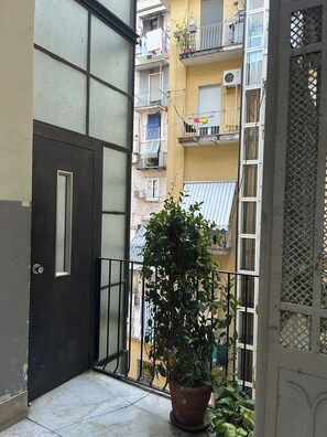 A balcony with a potted plant, a closed door, and a view of a yellow building with balconies. - Toledo Loft San Liborio (Napoli)