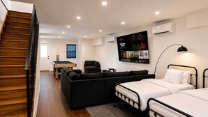 Habitación de hotel moderna con una escalera de madera, una mesa de billar, un sofá, dos camas y un televisor montado en la pared mostrando un cartel de película.