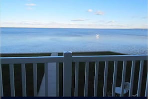 Vista desde un balcón sobre un mar tranquilo, con barandilla blanca y una silla.