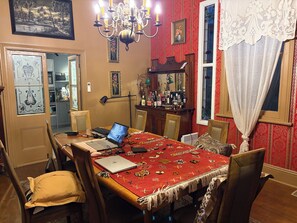 Un coin repas avec une nappe rouge, des chaises en bois, un lustre et une cuisine en arrière-plan.