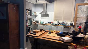 A kitchen with a wooden countertop, a hanging light fixture, a window with blinds, and a refrigerator.