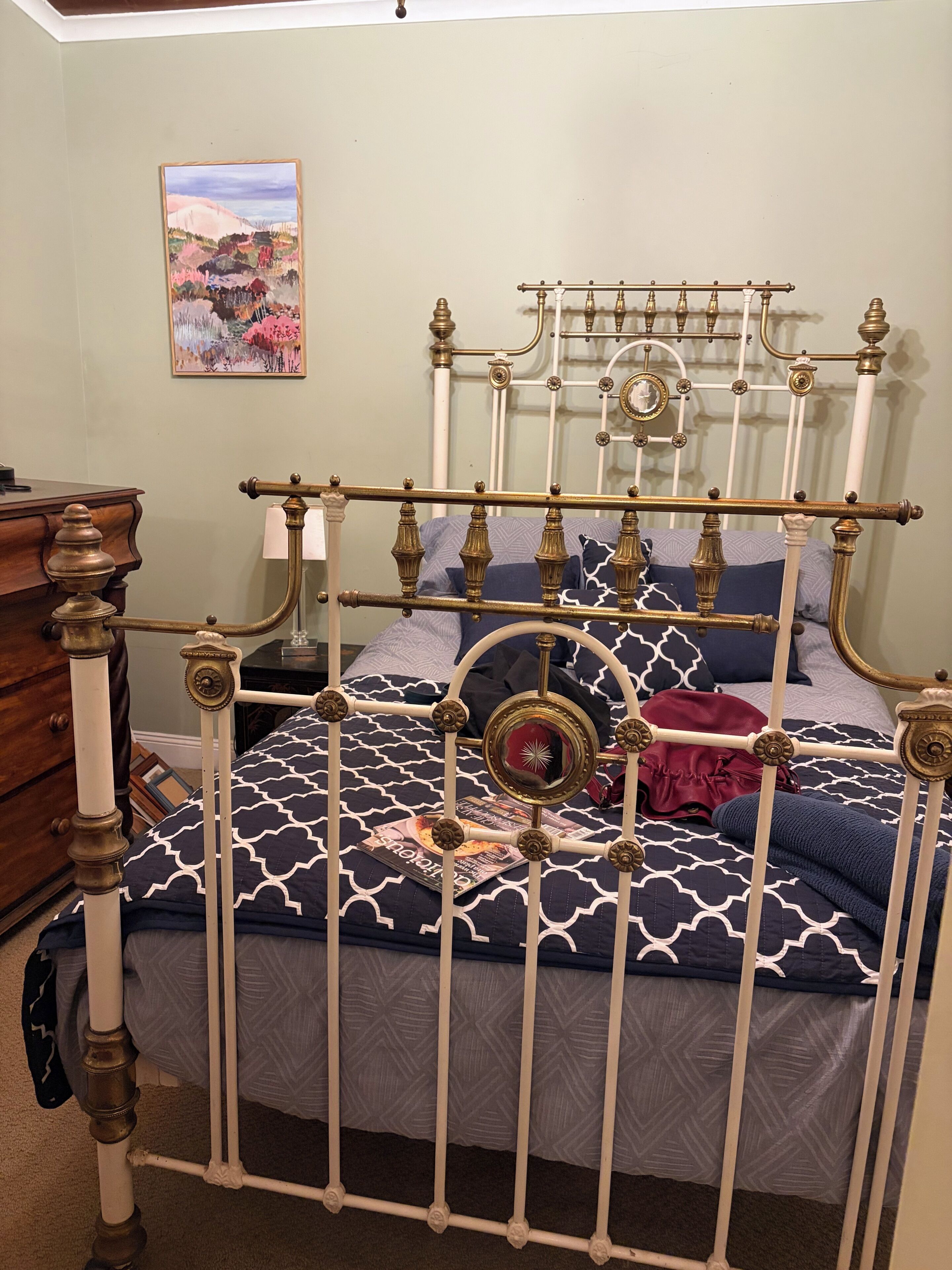 A bed with a metal frame, a patterned bedspread, and a decorative mirror.
