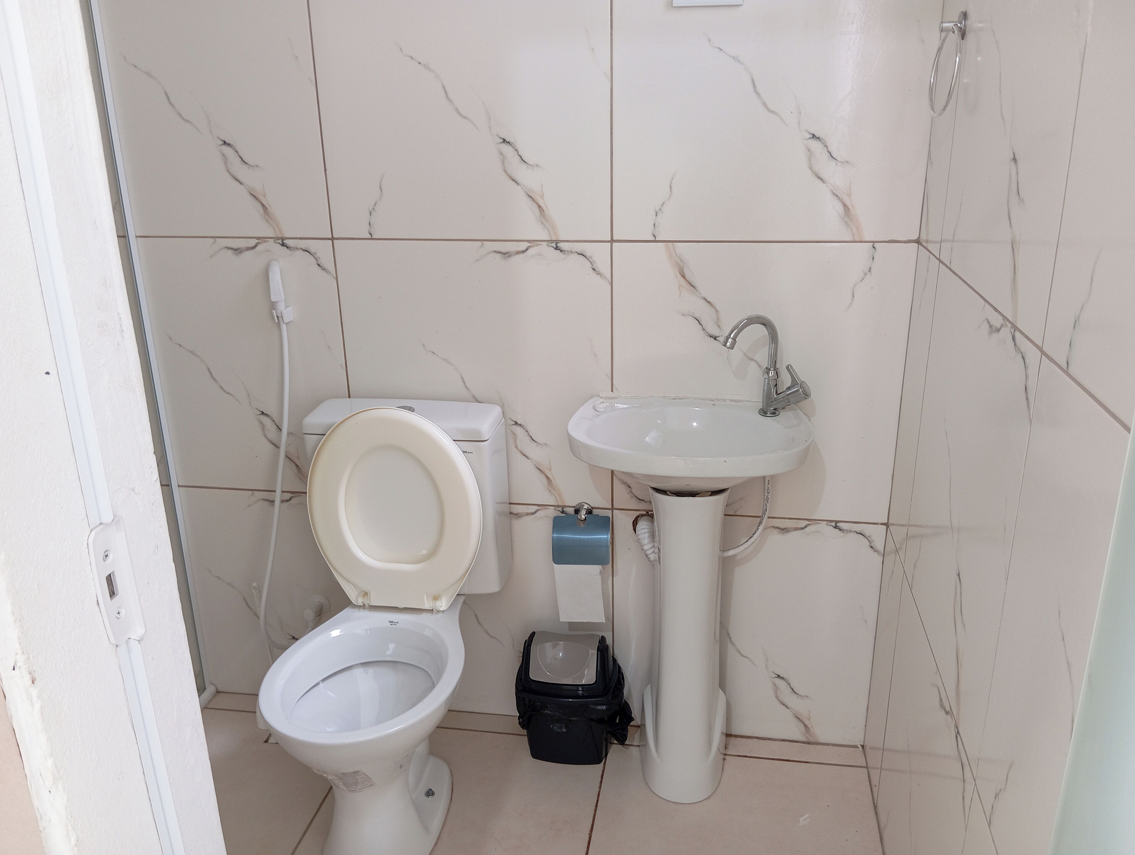 A bathroom with a toilet, sink, and a black trash bin.