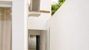 A clean, modern hallway with a glass door, a metal staircase, and a wall-mounted air conditioning unit.