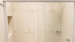 Ducha con cabezal de ducha manual, toallero de pared y un estante pequeño.