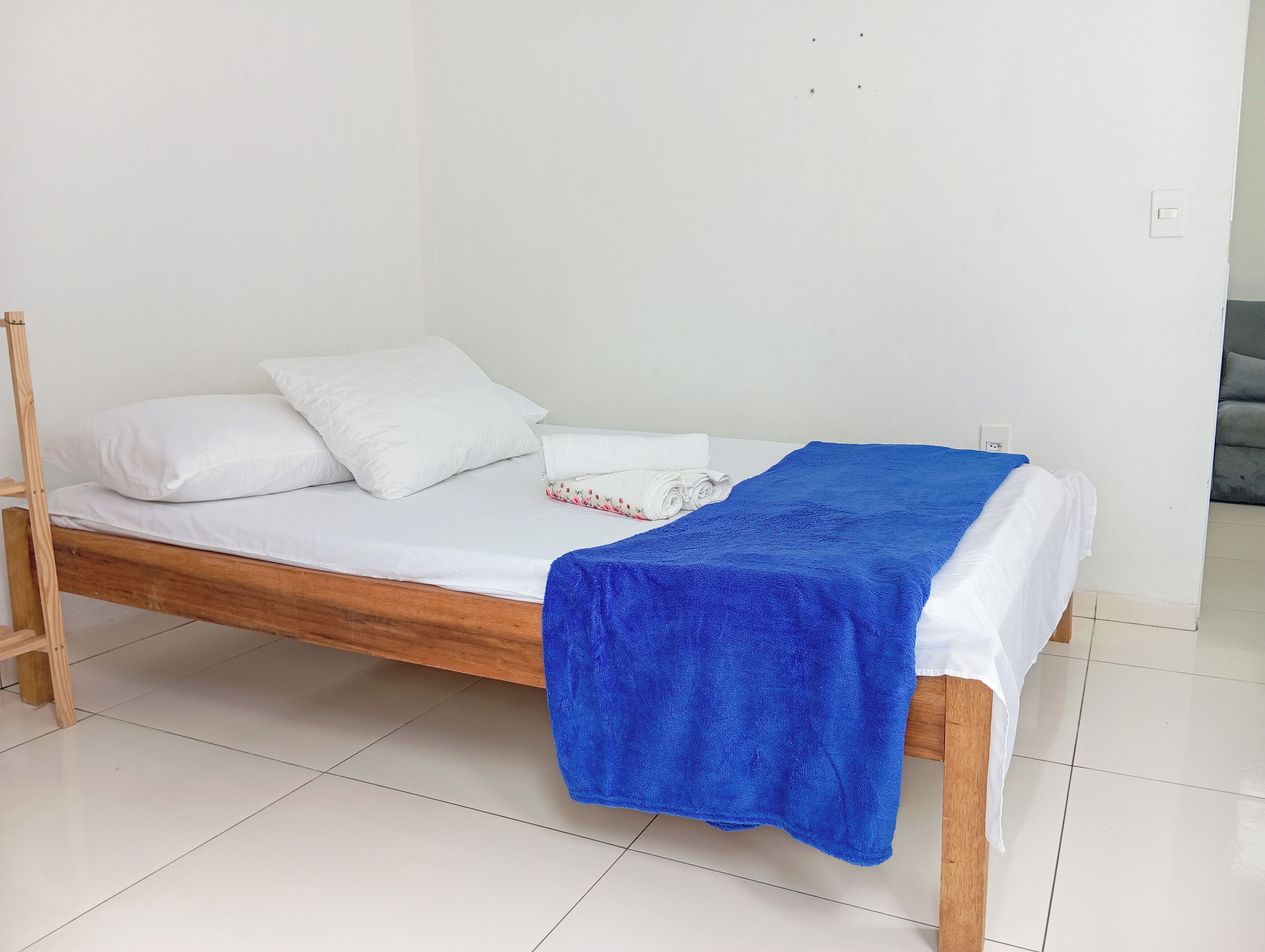 A single bed with white bedding, a blue blanket, and a rolled towel.