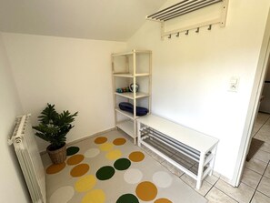 A room with a white radiator, a potted plant, a polka dot rug, a white bench, and a white shelving unit with a few items on it. - COUDERE House - SOUSTONS (SOUSTONS)