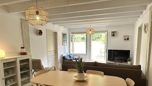 A dining area with a wooden table and chairs, a sofa, a television, and a window with a view of greenery. - COUDERE House - SOUSTONS (SOUSTONS)