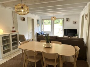 A dining area with a wooden table and chairs, a sofa, a television, and a window with a view of greenery. - COUDERE House - SOUSTONS (SOUSTONS)
