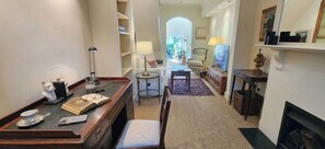 A hotel room with a desk, chair, bookshelf, armchair, and fireplace. - Paddington Central Sydney - Sunlit Courtyard (Paddington)