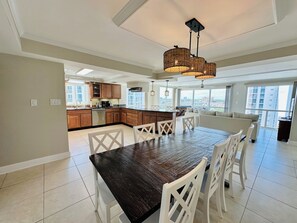 A spacious kitchen with wooden cabinets, a dining table with chairs, and a large window offering a city view. - Beachfront 3 br at Shoreline Towers on 9th floor offering great views for miles (Destin)