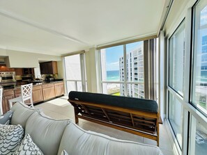 A modern living room with a large window, a sofa, and a wooden bench. - Beachfront 3 br at Shoreline Towers on 9th floor offering great views for miles (Destin)