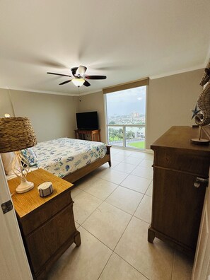 Ein Schlafzimmer mit einem Bett, einem Fernseher, einem Deckenventilator, einem Fenster mit Blick und einer Holzkommode.