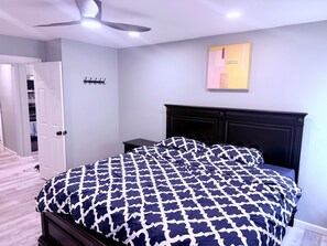 Ein Schlafzimmer mit einem Bett, einem Deckenventilator, einem Nachttisch, einem Wandbild und einem Schrank mit Tür.