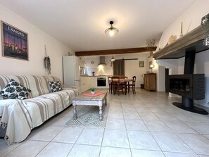 A living room with a sofa, a dining table with chairs, a kitchen in the background, and a fireplace. - BOURSAOU - PONTONX-SUR-L'ADOUR (PONTONX SUR L'ADOUR)