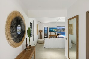 A modern hotel room with a large TV, a bed, a small table with a plant, and a view of the sea. - AURÉLIO SKY VIEW ST. BARTHÉLÉMY, PINEL, AND CUL DE SAC BAY (saint martin)