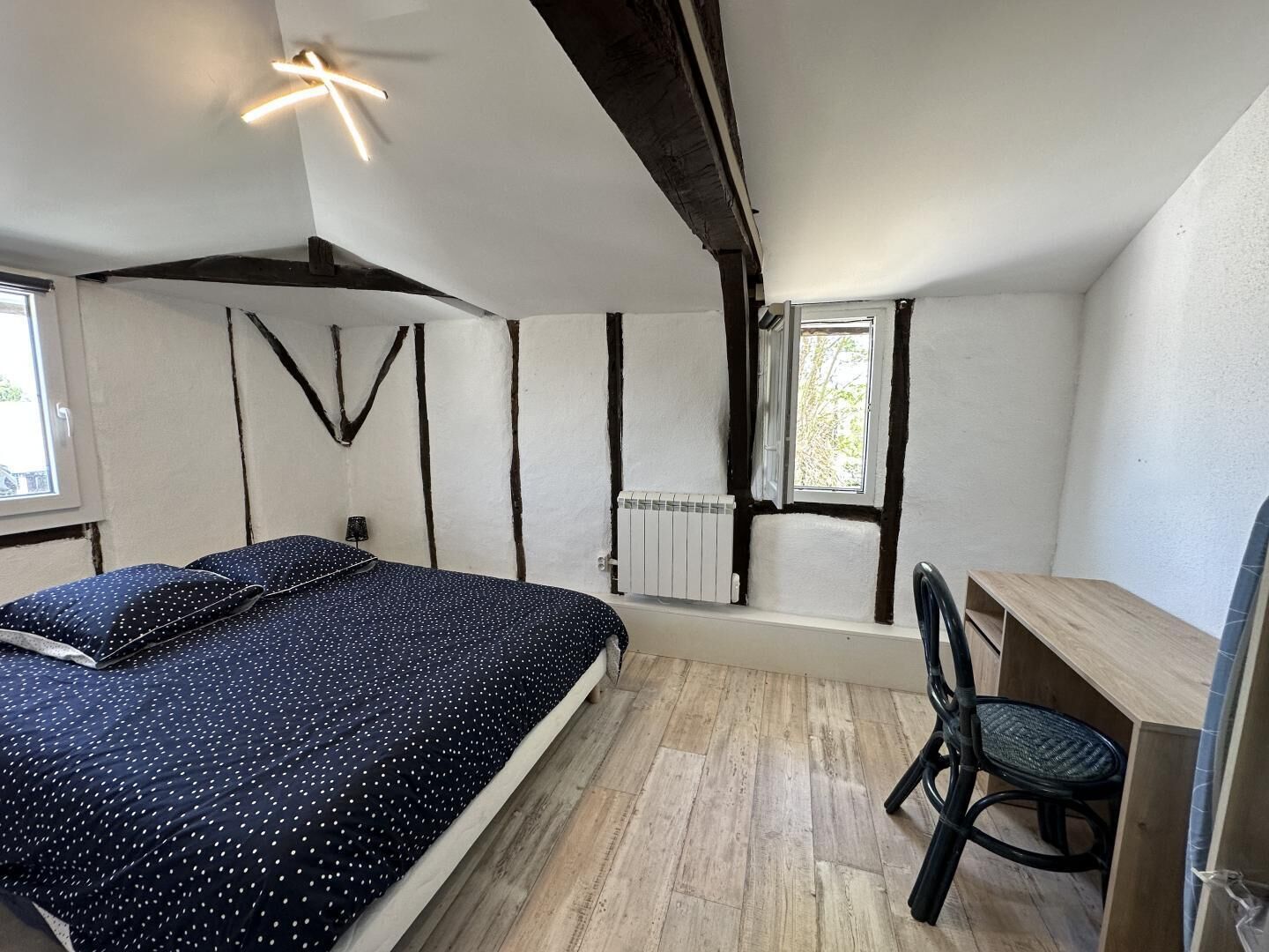 A bedroom with a bed, a desk, a chair, a radiator, and a window.