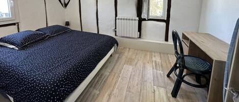 A bedroom with a bed, a desk, a chair, a radiator, and a window.