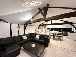 A modern loft-style living space with exposed wooden beams, a black leather sofa, a dining area, and a kitchen. - PATXI - DAX - City Break (DAX)