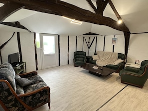 Ein Zimmer mit freiliegenden Holzbalken, einem Sofa, zwei Sesseln, einem Couchtisch und einem Fernseher.