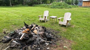 Ein Garten mit Feuerstelle, zwei Adirondack-Stühlen und einem kleinen Tisch.
