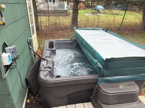 A hot tub with a cover, a power outlet, and a green fence in the background. - Easy walk to lake, shops & restaurants, HOT TUB (Rangeley)