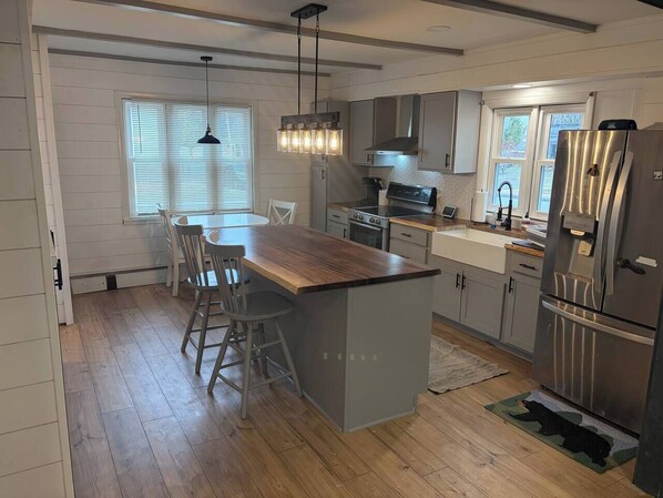 A modern kitchen with a central island, stainless steel appliances, and a dining area with a wooden table and chairs. - Easy walk to lake, shops & restaurants, HOT TUB (Rangeley)