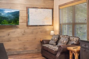 Un intérieur en bois avec un canapé, une carte accrochée au mur et une fenêtre équipée de stores.
