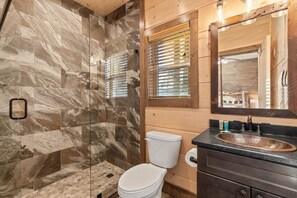 Une salle de bain dotée d’une douche à parois de verre, de toilettes blanches, d’un meuble-lavabo en bois et d’un grand miroir.