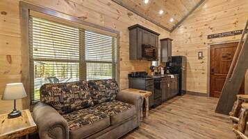 A cozy cabin interior with a sofa, wooden walls, a kitchen area, and a sign indicating the Appalachian Trail.