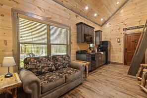 A cozy cabin interior with a sofa, wooden walls, a kitchen area, and a sign indicating the Appalachian Trail. - Trailhead Lodge #13 Loft + Fire Pit (Cosby)