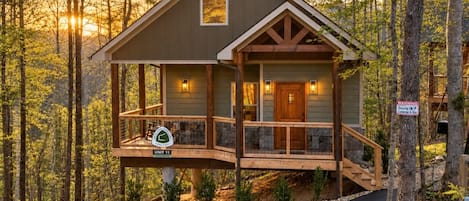 A cabin with a deck, surrounded by trees, and a sign indicating a unit number.