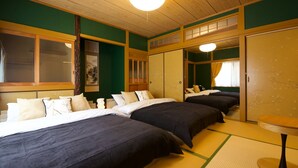 Habitación de hotel con tres camas, suelo de estera de tatami, puerta corredera japonesa tradicional y una pequeña mesa redonda.