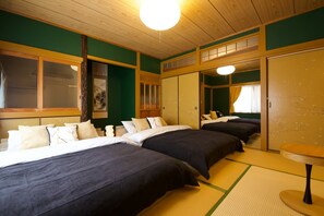 Quarto de hotel com três camas, piso de esteira de tatame, porta japonesa tradicional deslizante e uma pequena mesa redonda.