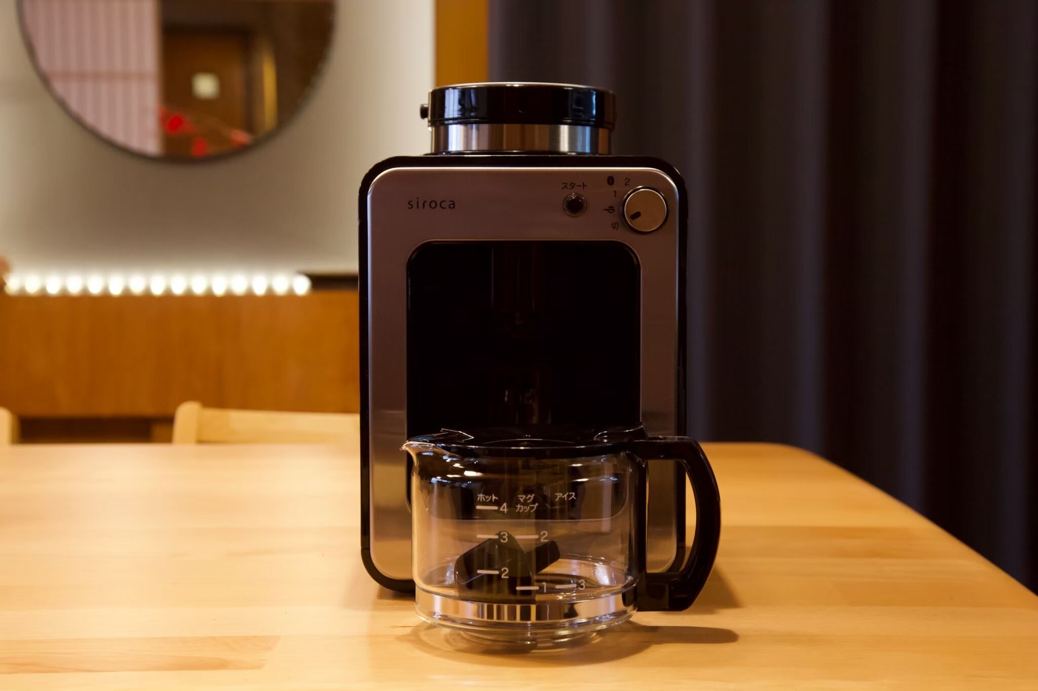 Eine Kaffeemaschine von Siroca steht auf einem Holztisch, vor ihr ein messbarer Messbecher.