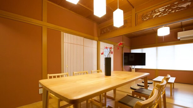 A traditional Japanese-style room with tatami flooring, a wooden dining table, and a TV.