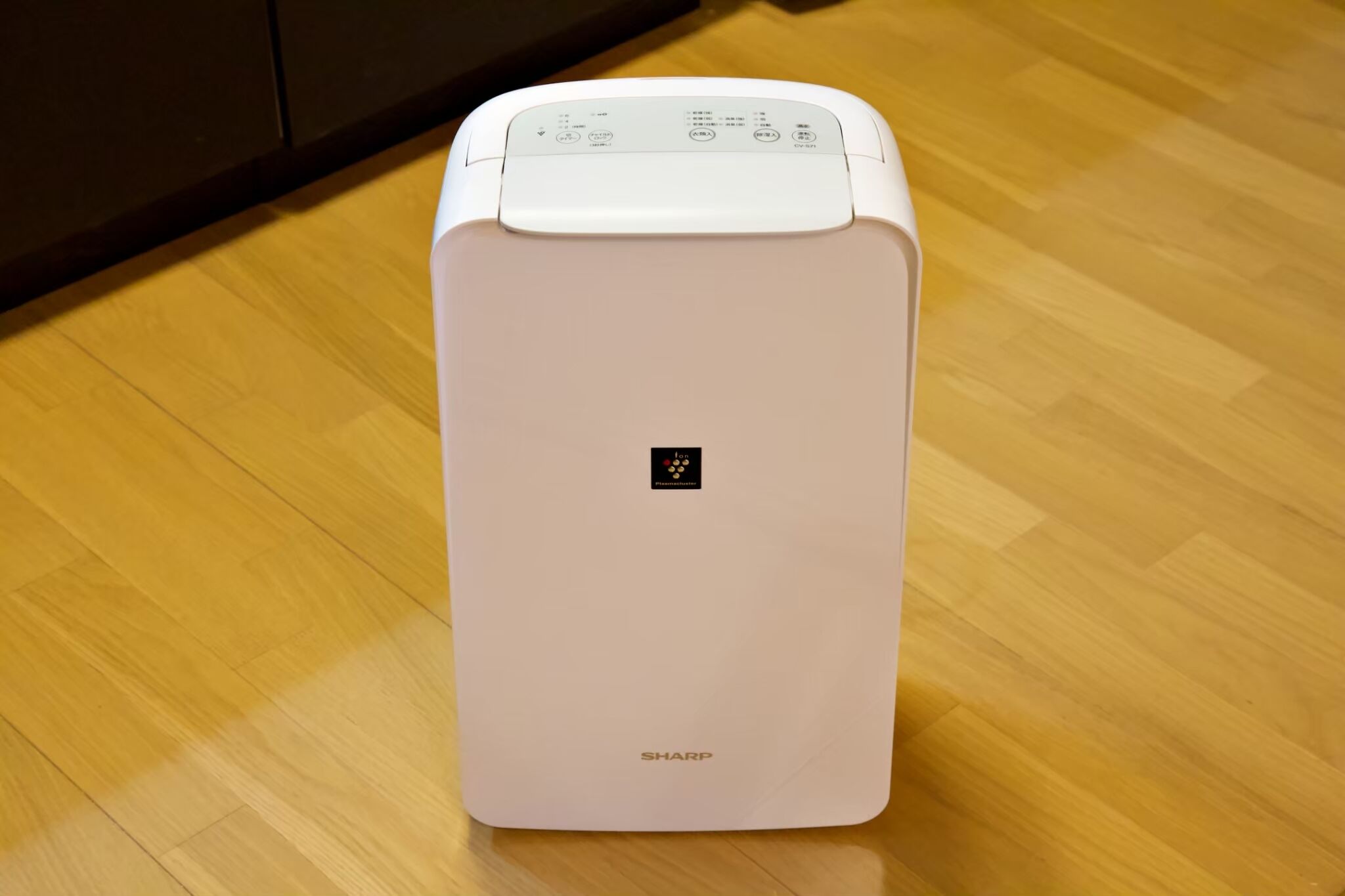 A white, modern, compact appliance with a control panel on top, placed on a wooden floor.