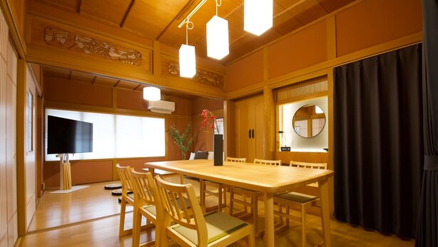 Una habitación tradicional japonesa con una mesa de comedor de madera, sillas, un televisor de pantalla plana y un espejo grande.